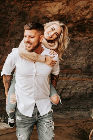 Joyful piggyback moment captured against textured rock wall outdoors.