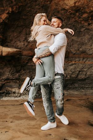 Couple sharing intimate embrace against rustic rock formation backdrop.