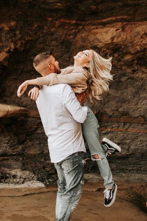 Carefree couple spinning and laughing against dramatic rocky backdrop.