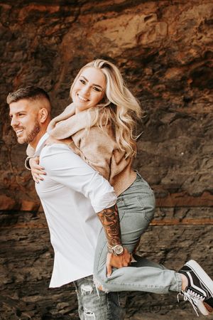 Adventurous couple enjoying playful piggyback ride near rocky cliffs.