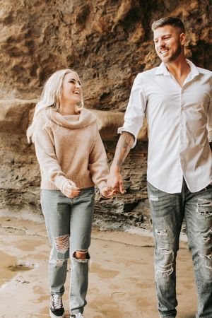 Couple laughing while walking hand in hand along rocky terrain.