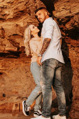 Romantic couple embraces against red rock formations in warm sunlight.