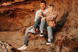 Casual couple sits together on rocky ledge during sunset photoshoot.