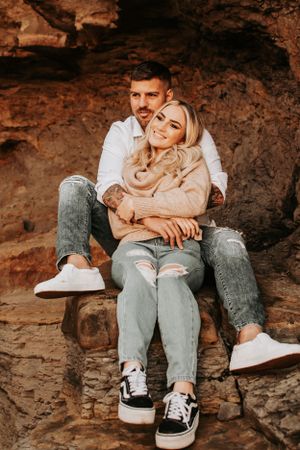 Couple snuggles together on rocky outcrop wearing casual denim and sneakers.