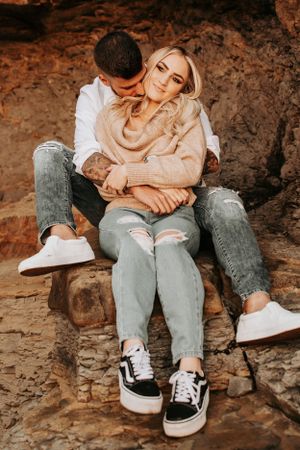 Intimate moment between couple sitting on rocky ledge wearing casual attire.