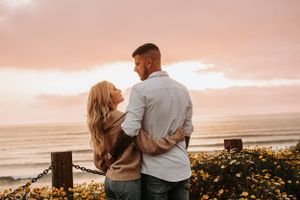 Couple shares intimate moment against pink sunset sky with ocean view.