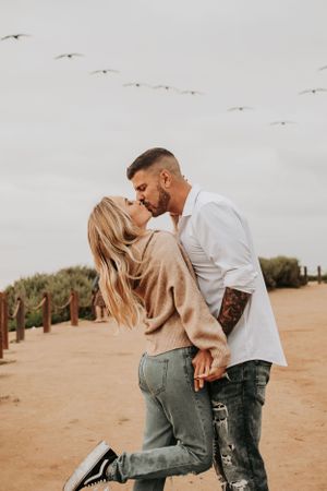 Romantic moment captured on sandy path with yellow flowers and wooden fence.