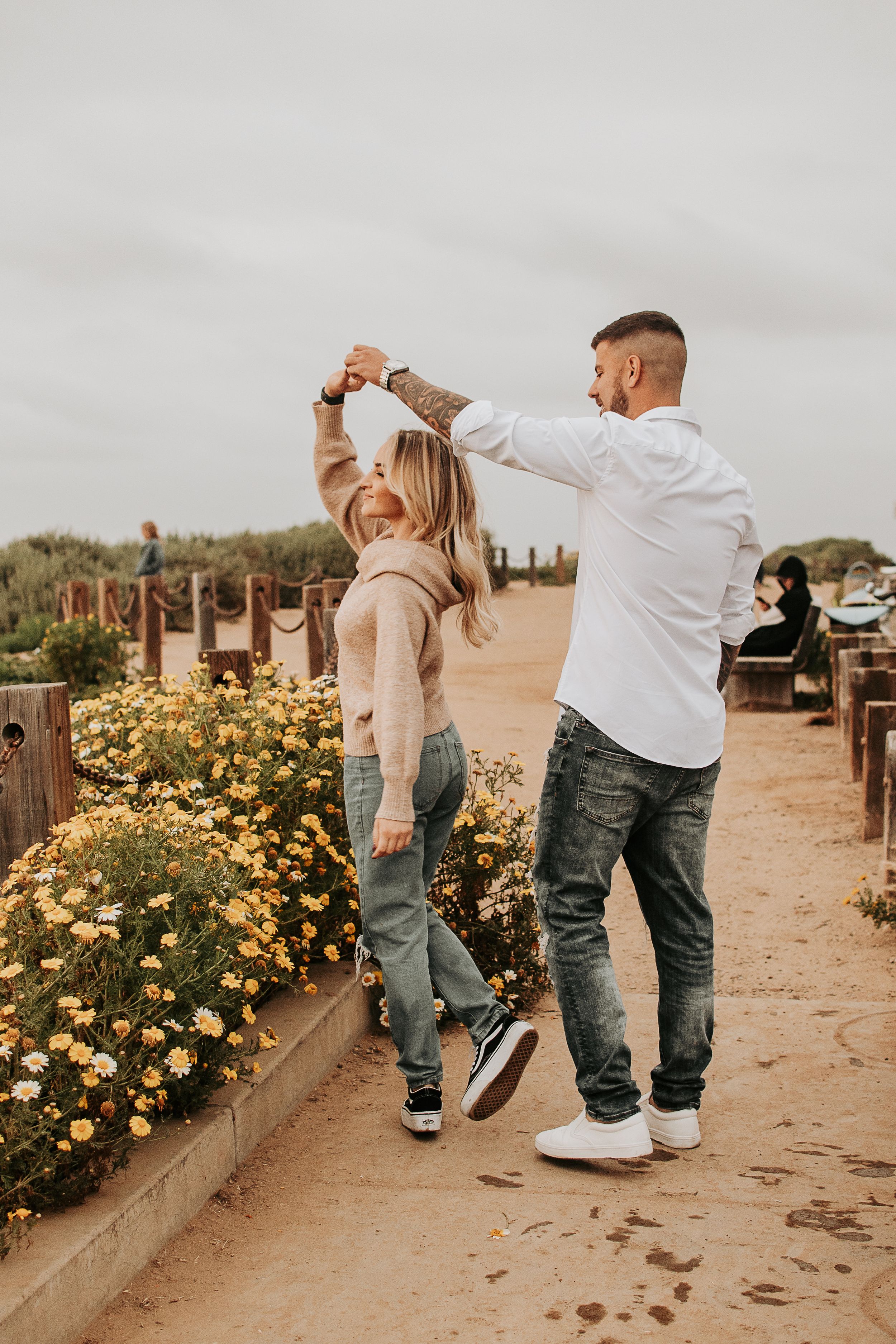 Playful dancing moment on sandy path with blooming yellow flowers.