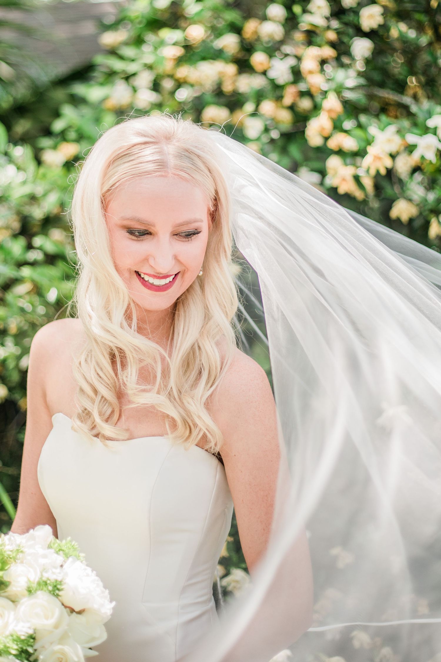 A radiant bride with flowing veil smiles in a garden setting.