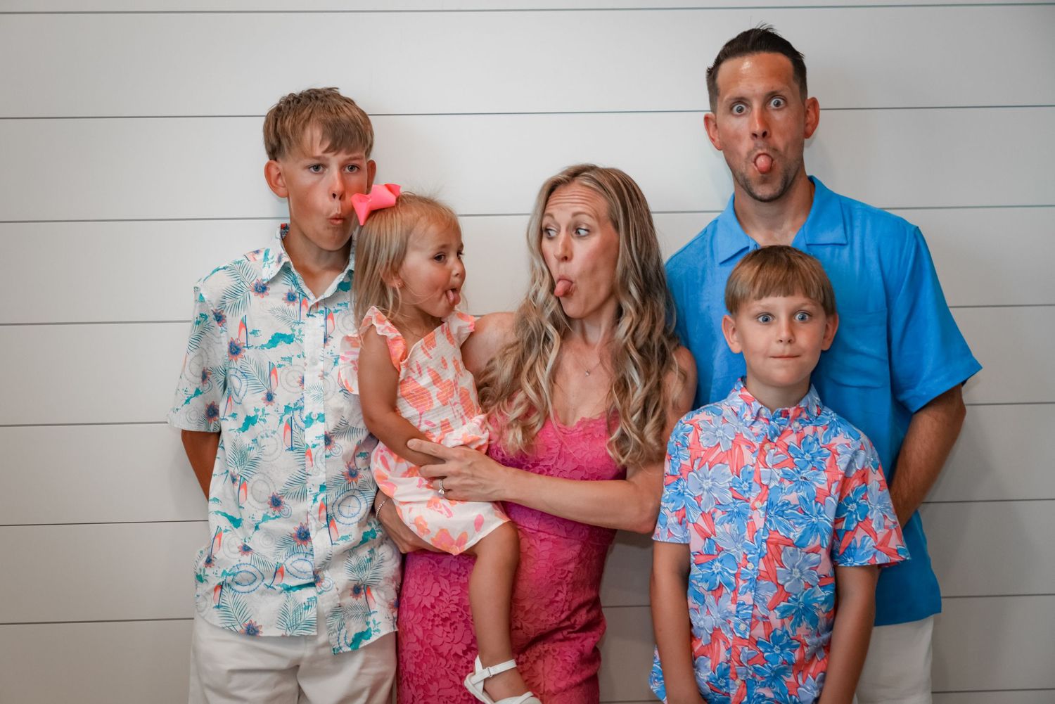 Family portrait with silly expressions against a white shiplap wall background.