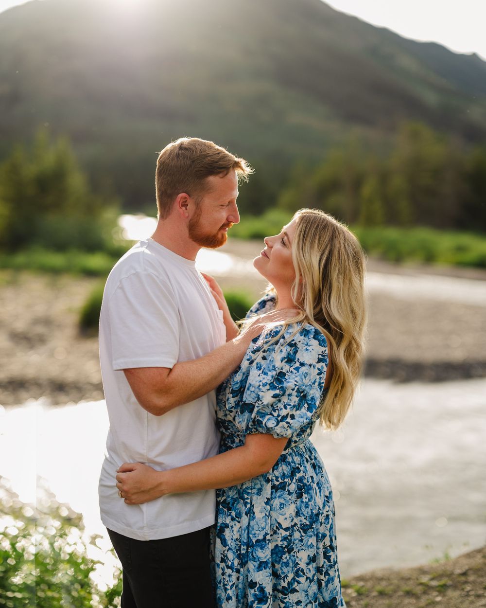 Couple embracing by a mountain stream in casual attire during golden hour.