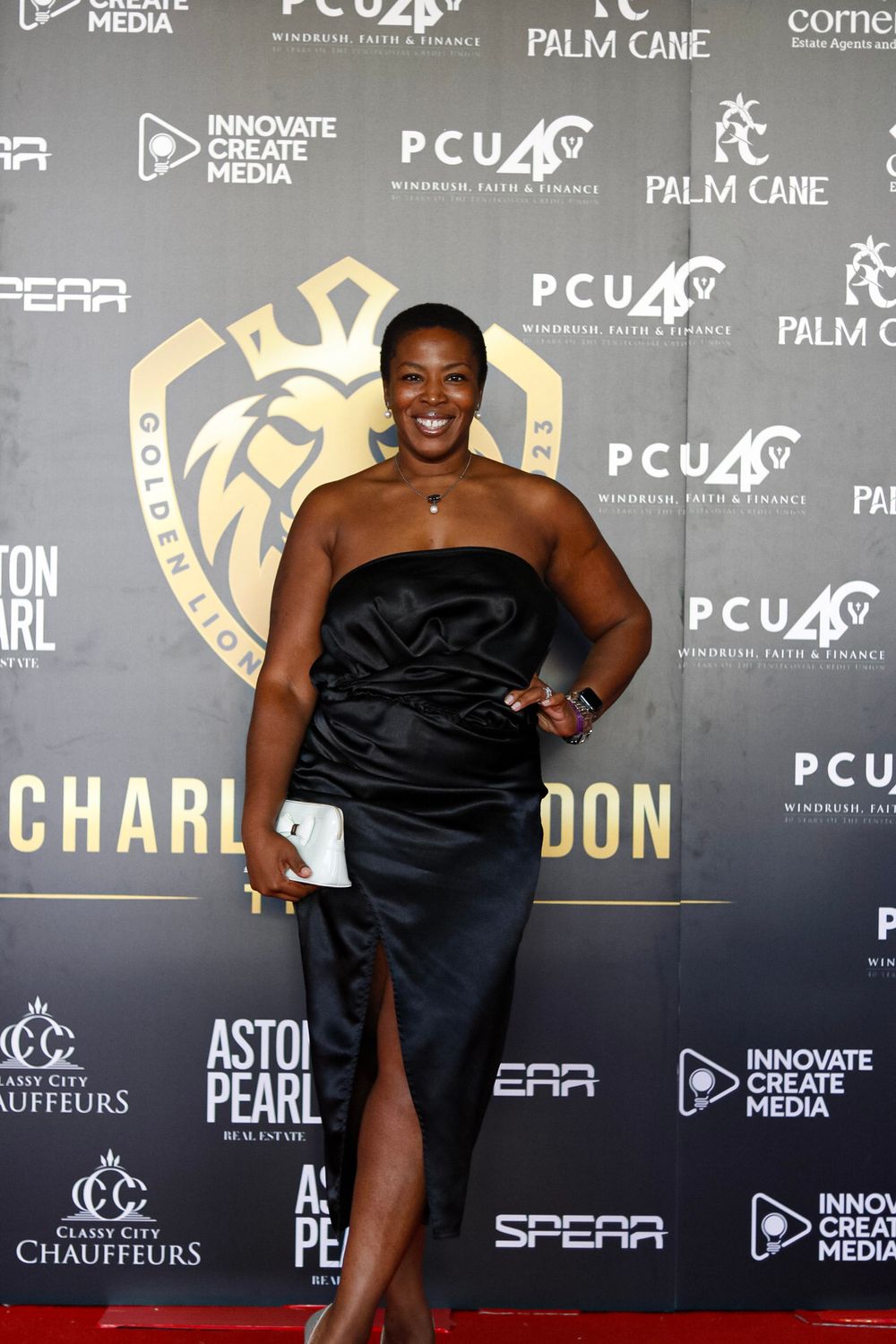 Elegant black strapless gown with thigh slit against branded step and repeat wall.