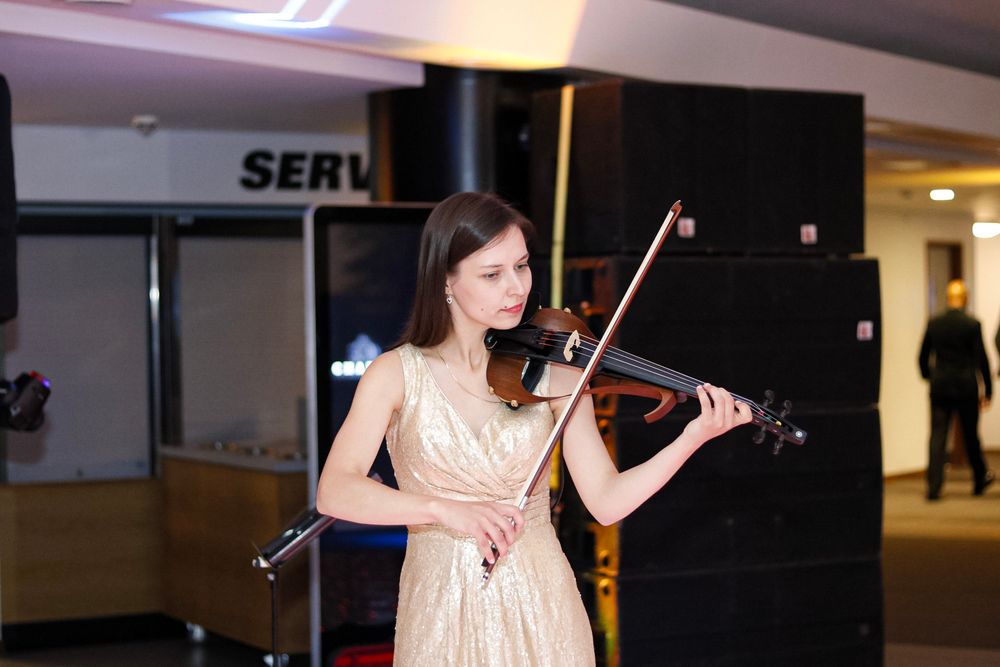 A violinist in an elegant cream dress performs in an indoor venue.