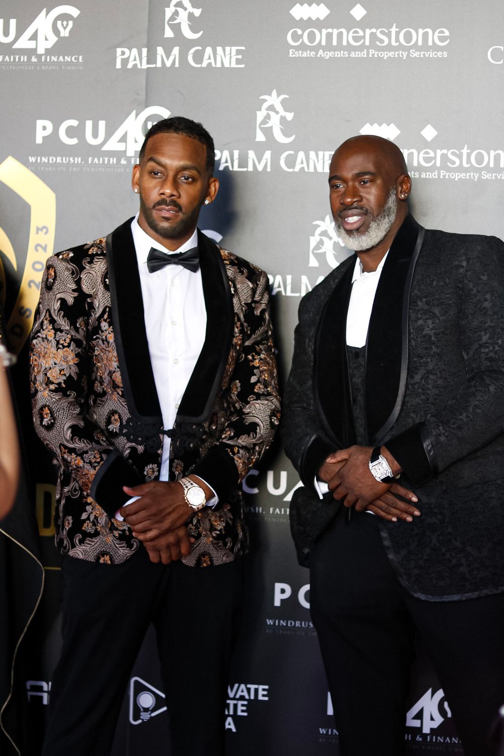 Two attendees in stylish tuxedos pose at a formal event.