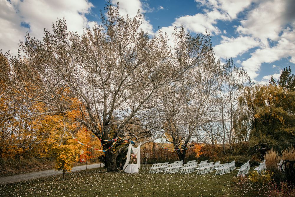 A fall outdoor wedding ceremony setup with white chairs and autumn foliage in the background.