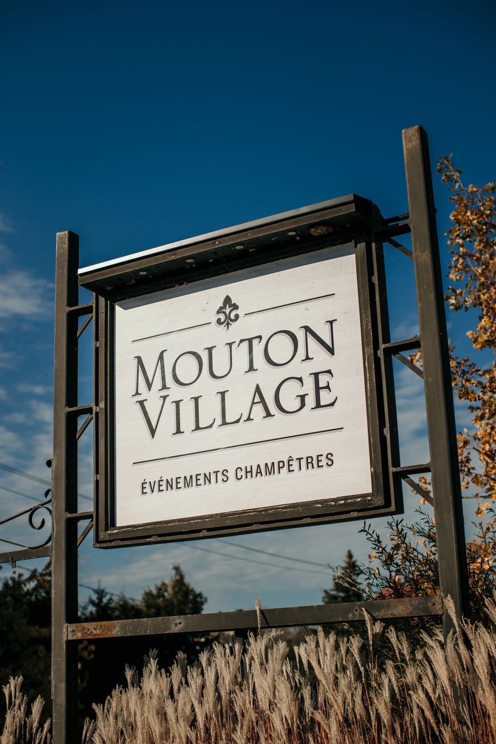 Rustic wooden sign for Mouton Village events venue against deep blue sky.