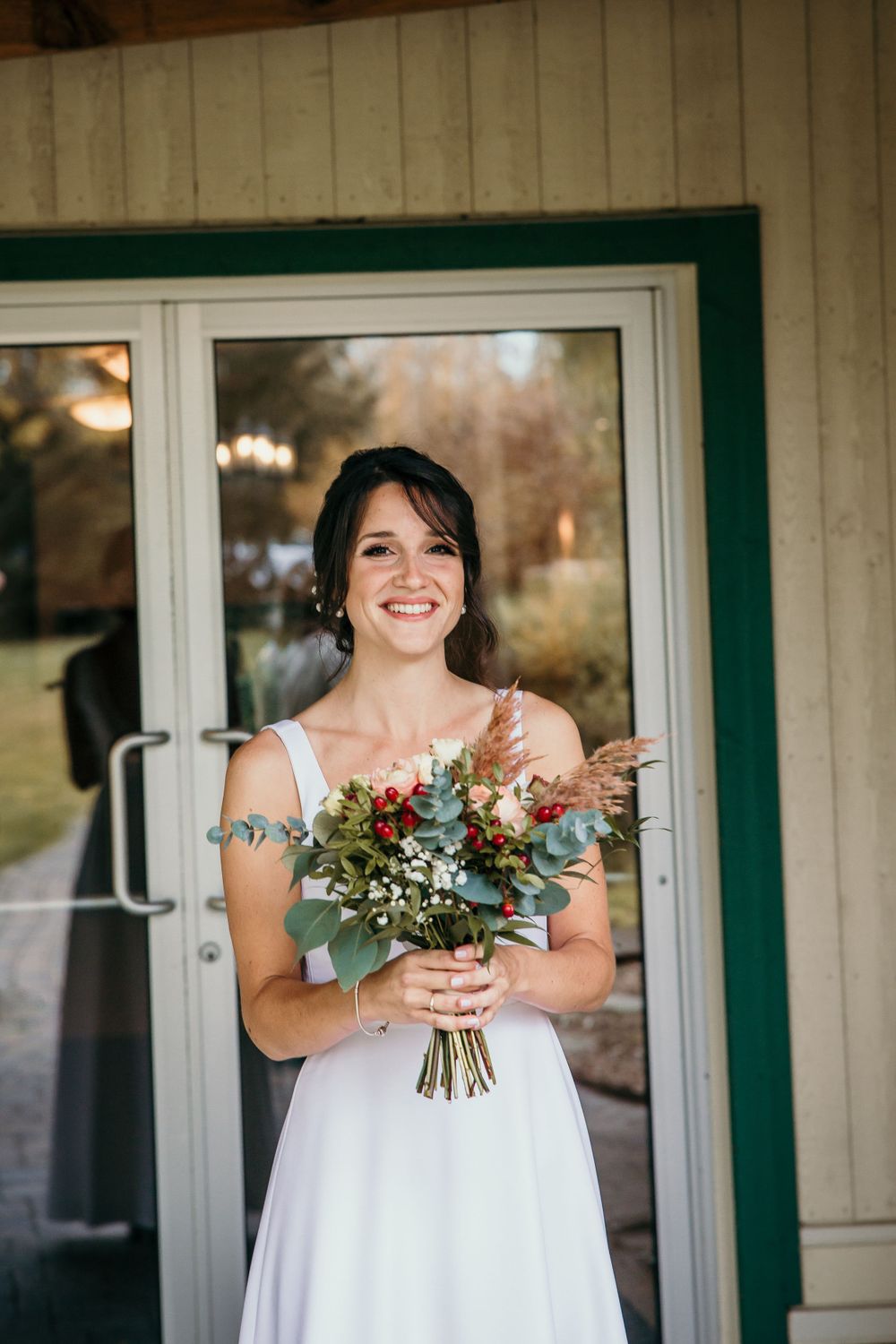 A bride in a white dress holds a beautiful bouquet of eucalyptus and wildflowers.