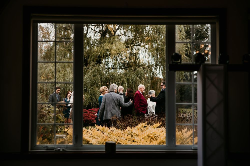 An outdoor wedding ceremony viewed through a window frame with fall foliage in the background.
