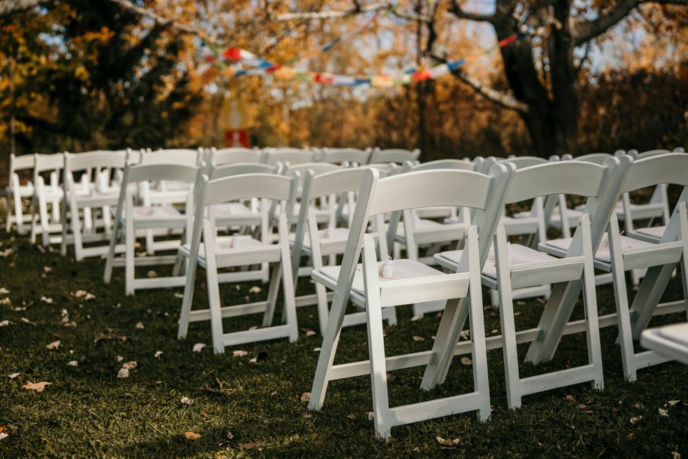 Rows of white folding chairs set up for an outdoor wedding ceremony with autumn trees in the background.
