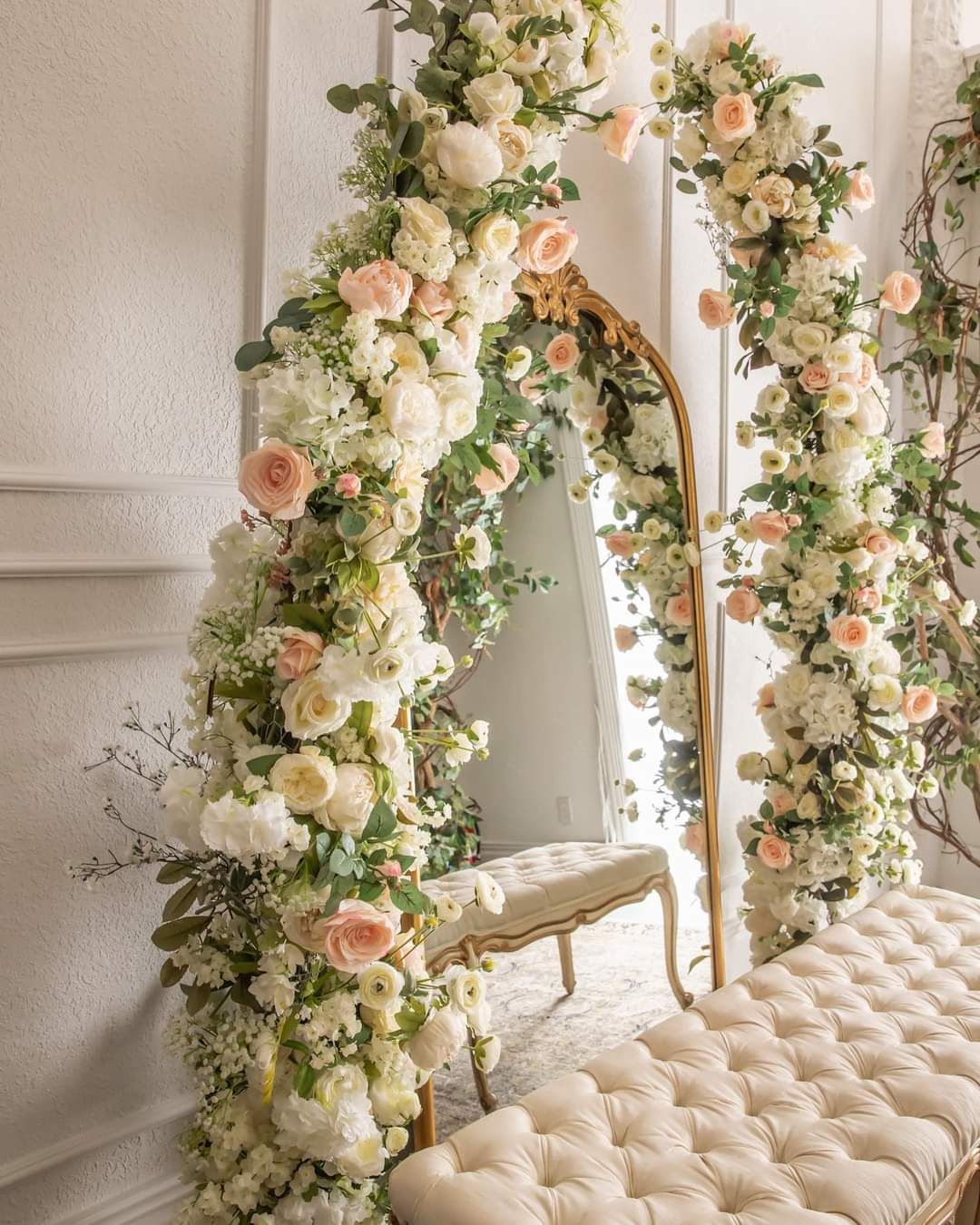 Luxurious floral arch with peach and white roses framing an elegant tufted bench.