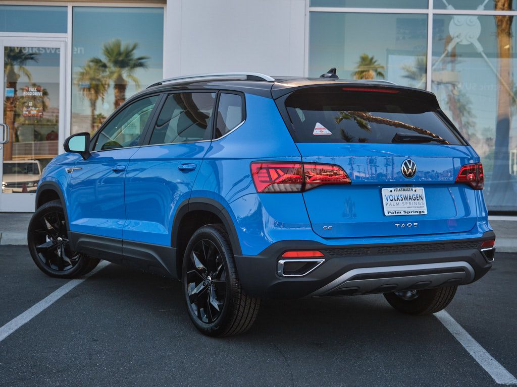 Rear three-quarter view of blue Volkswagen Taos SUV in dealership parking lot.