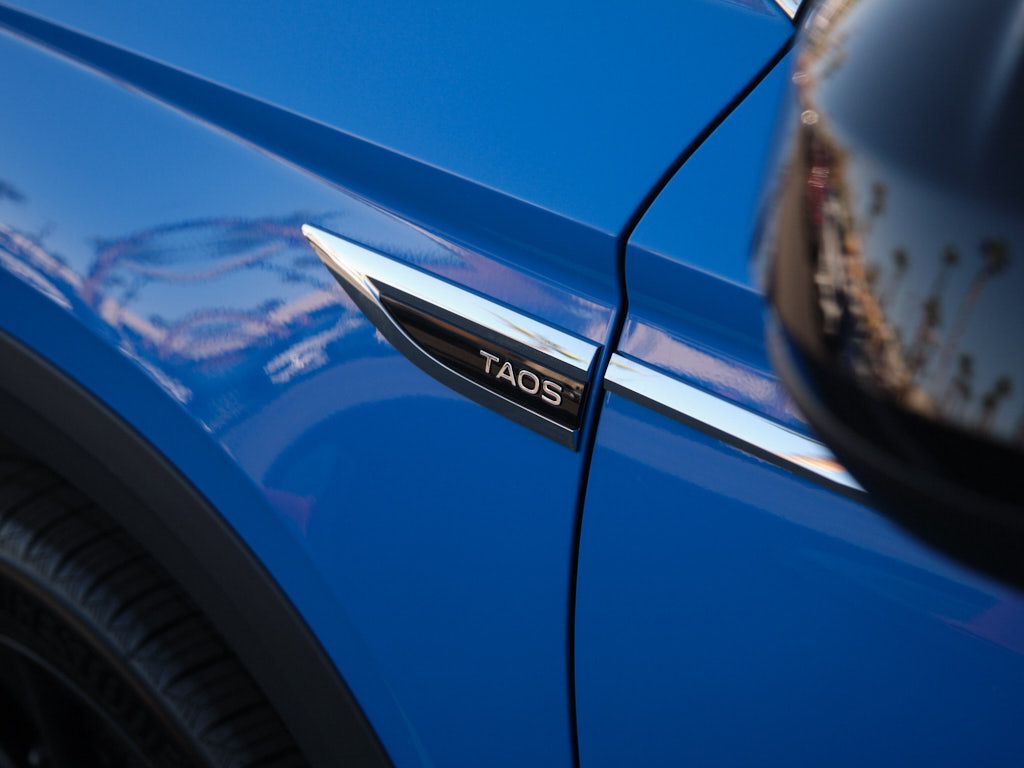 Close-up of a blue car's exterior panel displaying the Taos model badge.