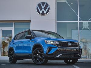 Blue Volkswagen Taos SUV parked in front of dealership with VW logo signage.