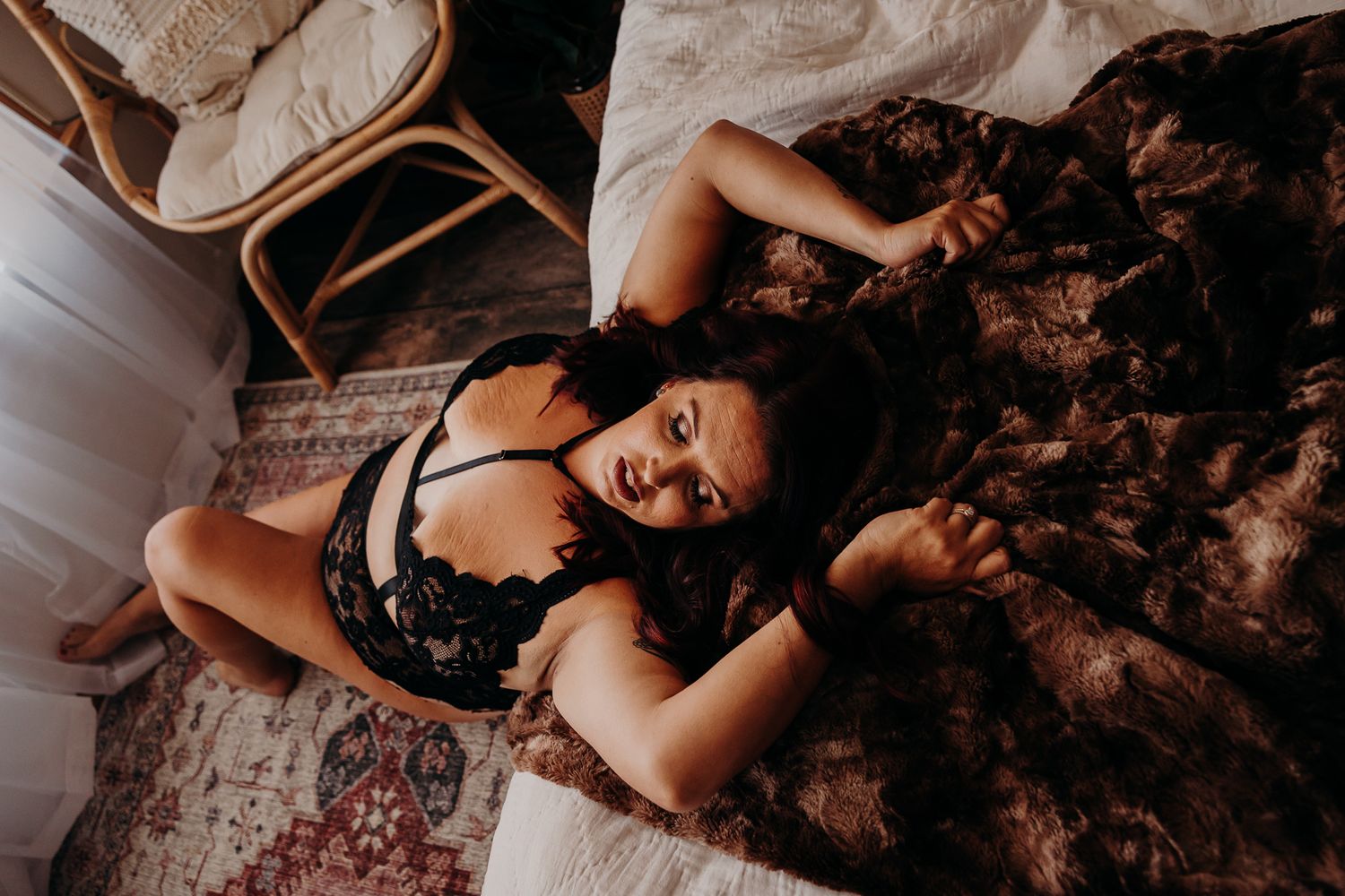 Brunette woman in black lace lingerie lying on a floral blanket on the floor.