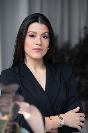 Professional headshot of woman in black blazer with elegant jewelry.