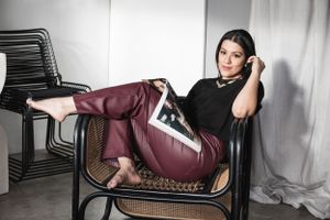A person lounging in a black cane chair wearing burgundy pants and a black top.