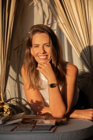 A person in a textured white top posed against dried palm fronds in warm lighting.