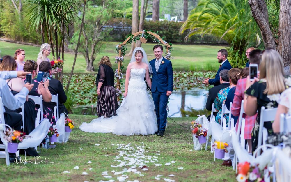 An outdoor wedding ceremony with flower petals scattered along the aisle and guests seated on white chairs.
