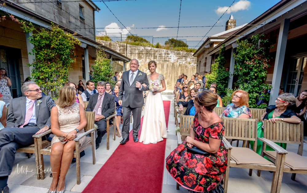 Wedding ceremony in a courtyard setting with red carpet and seated guests.
