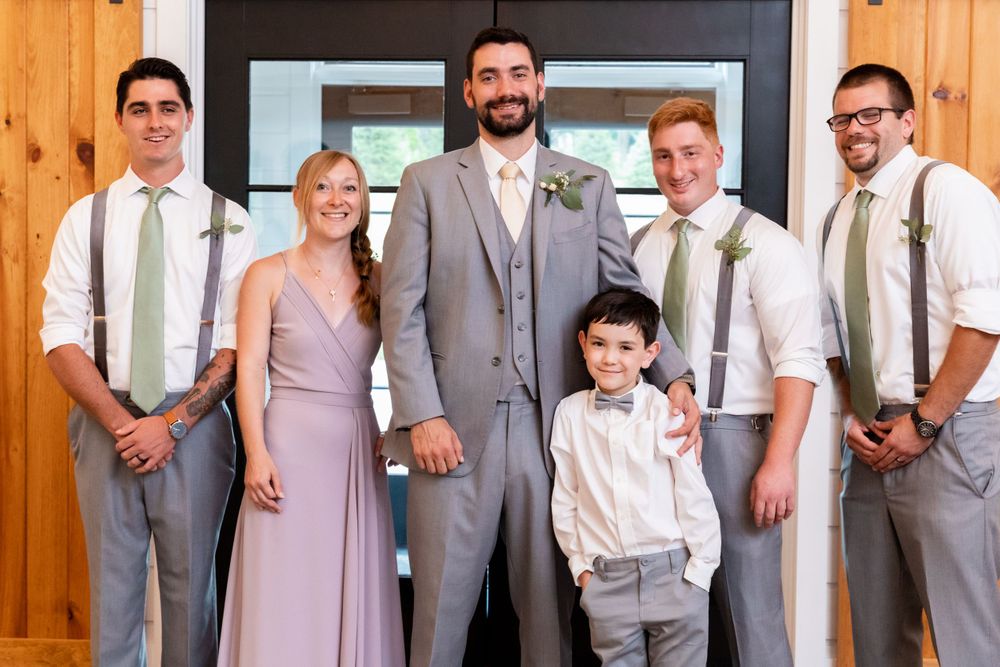 Wedding party members in gray and blush attire posing in front of wooden doorway.
