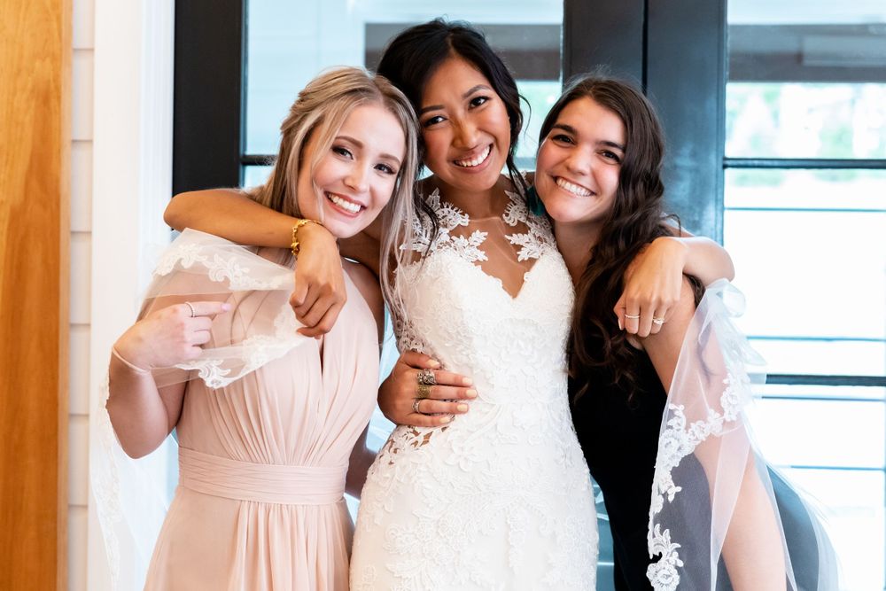 Three bridesmaids share a joyful moment together, wearing elegant dresses in blush and white tones.
