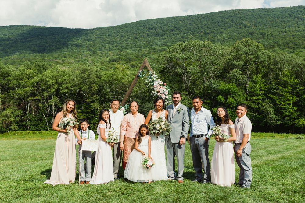 Wedding party gathered for group portrait on green lawn with mountains in background.