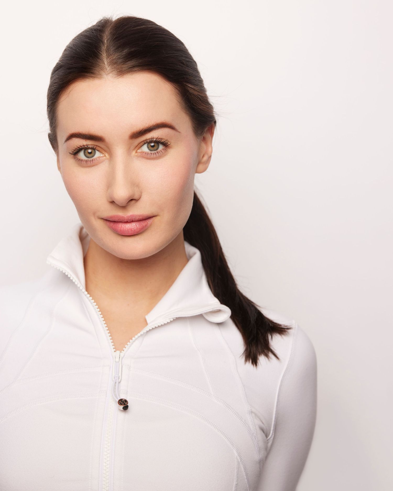 Professional portrait of a person with dark hair wearing a white zip-up top against a light background.