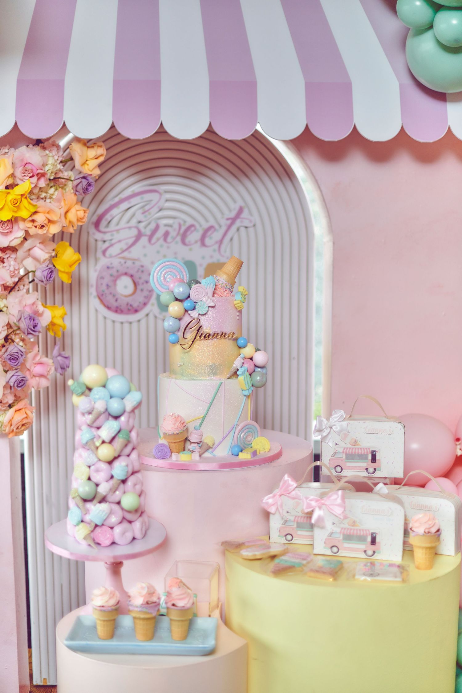 Pastel candy dessert table display with donuts, ice cream cones and sweets under a pink and white striped awning.