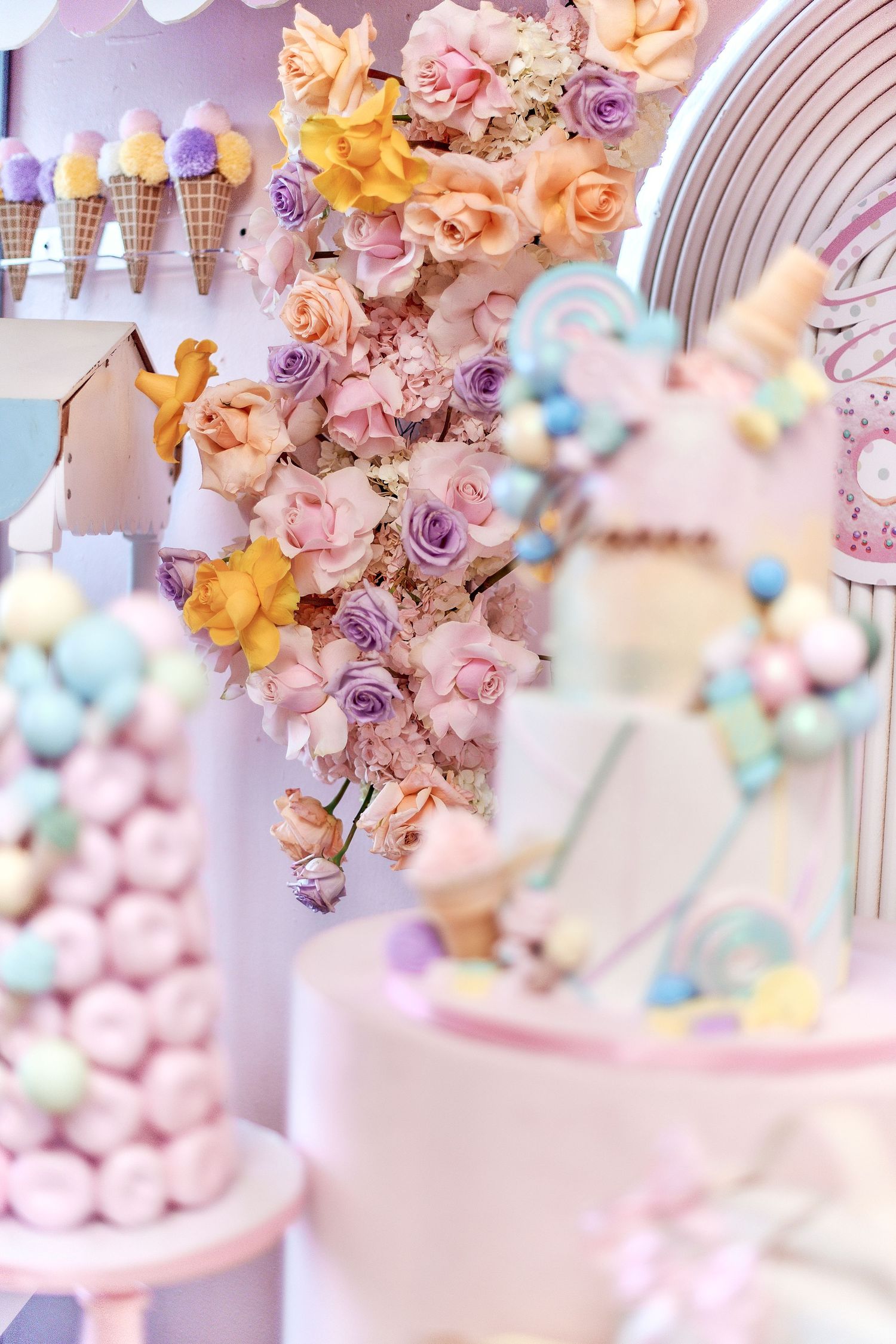 Pastel pink and purple floral decorations with roses adorn a dessert display featuring ice cream cones and party treats.
