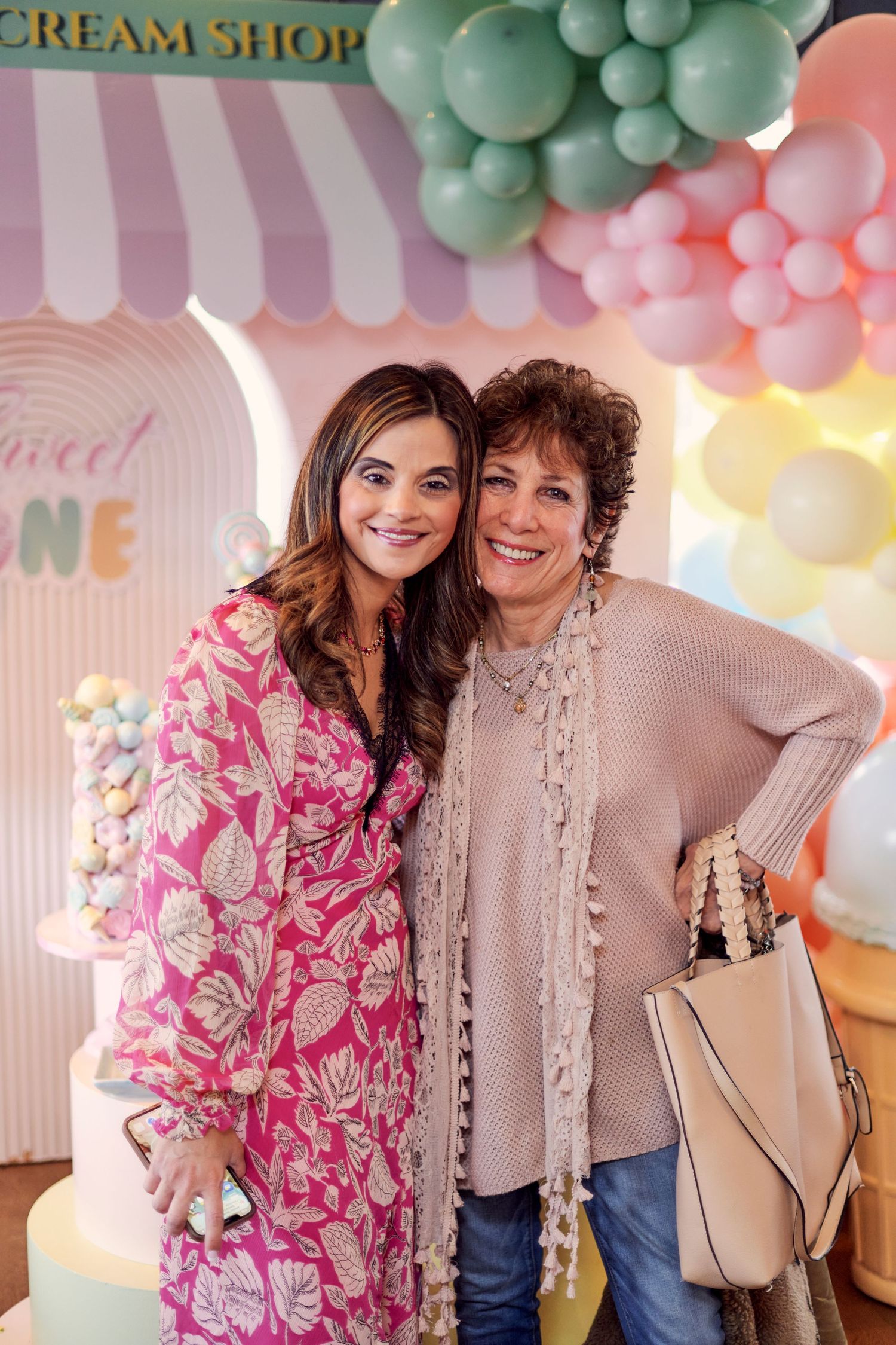 Two people posing together at a party with pastel balloon decorations and an ice cream shop backdrop.