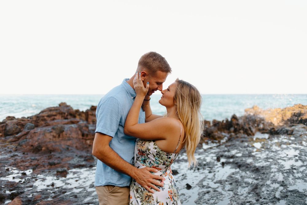 Couple in casual summer outfits sharing romantic moment on rocky beach.