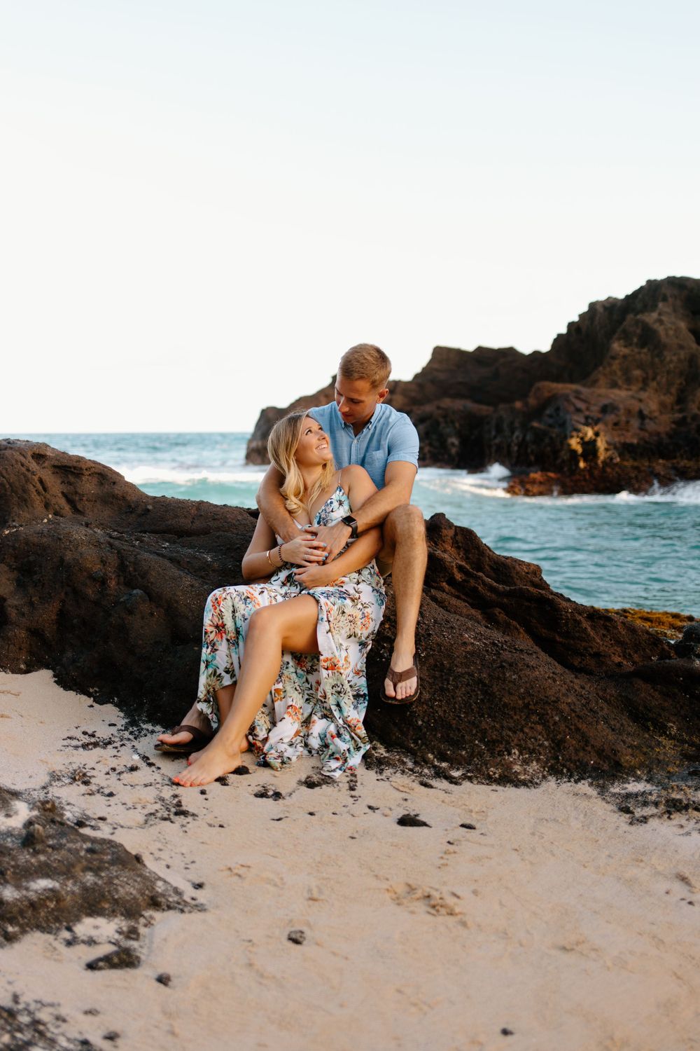 Couple cuddling on volcanic rocks at beach during golden hour.
