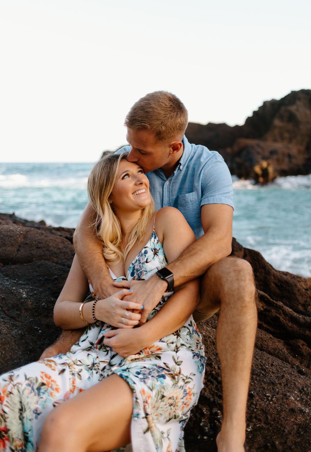 Intimate couple sharing tender moment while sitting on coastal rocks by ocean.