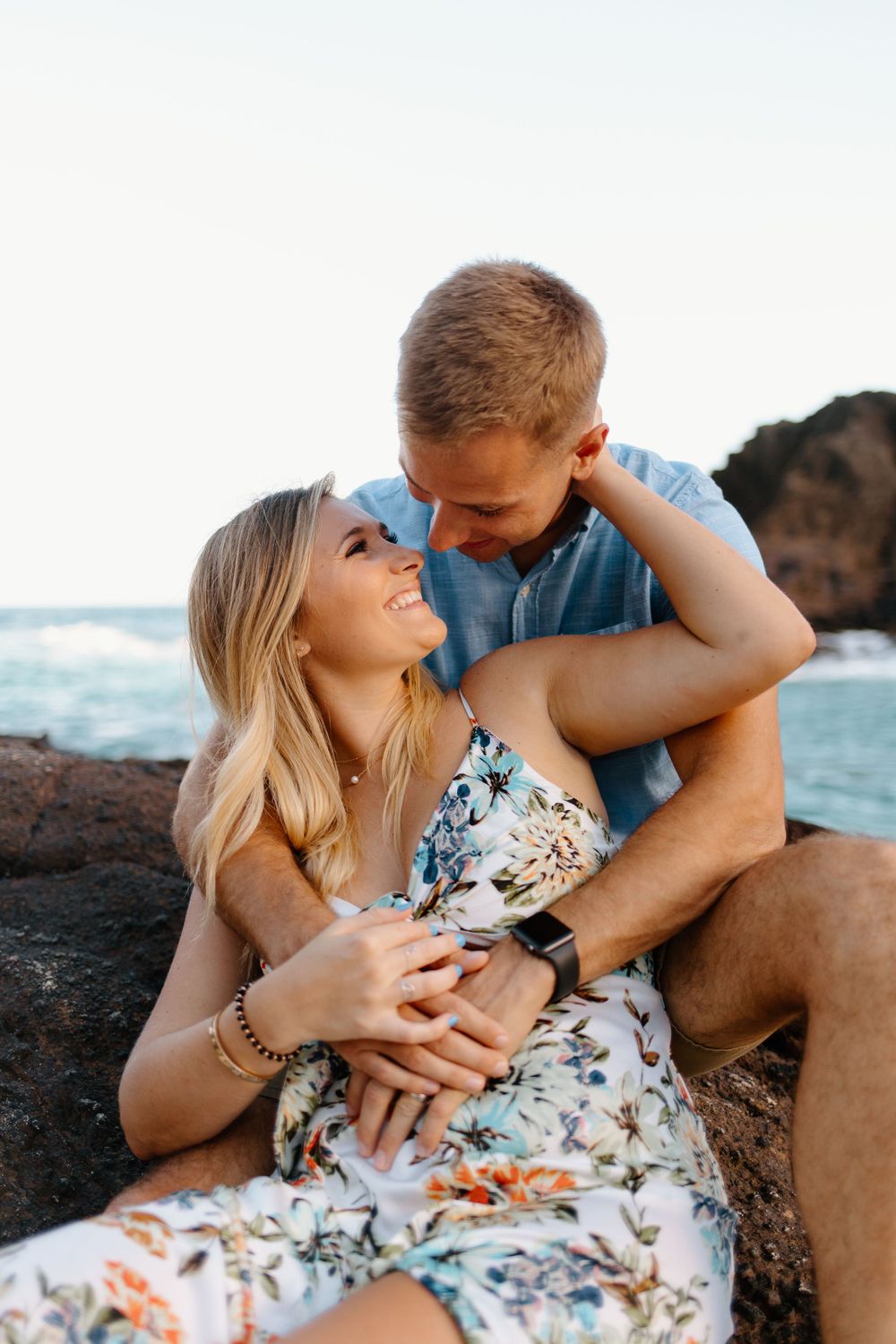 Couple shares intimate moment while sitting on coastal rocks at sunset.