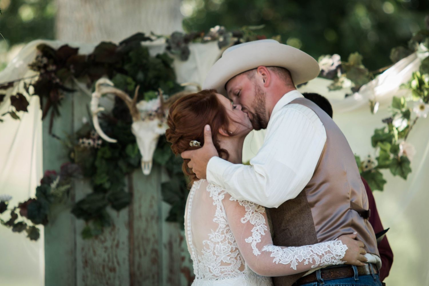 A couple shares romantic moments in their wedding attire under a lush green garden setting.