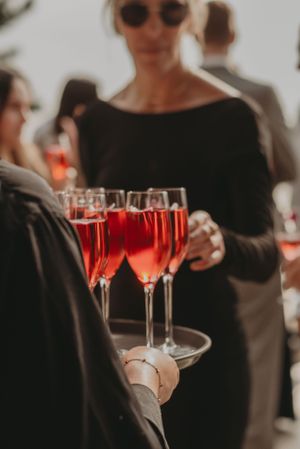 A tray of rose-colored champagne being served at an outdoor gathering.