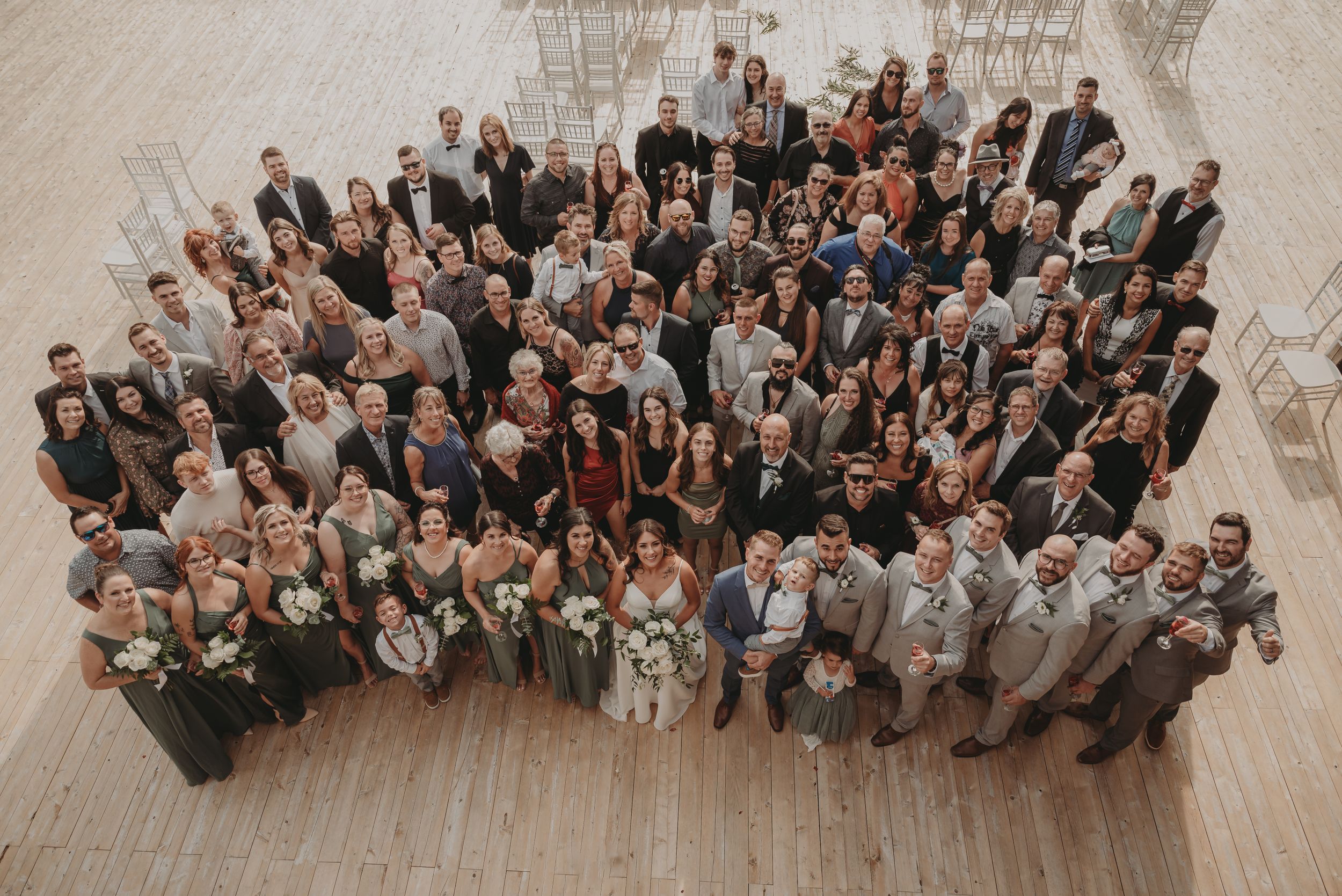 Overhead view of large wedding party and guests gathered for formal group photo indoors.
