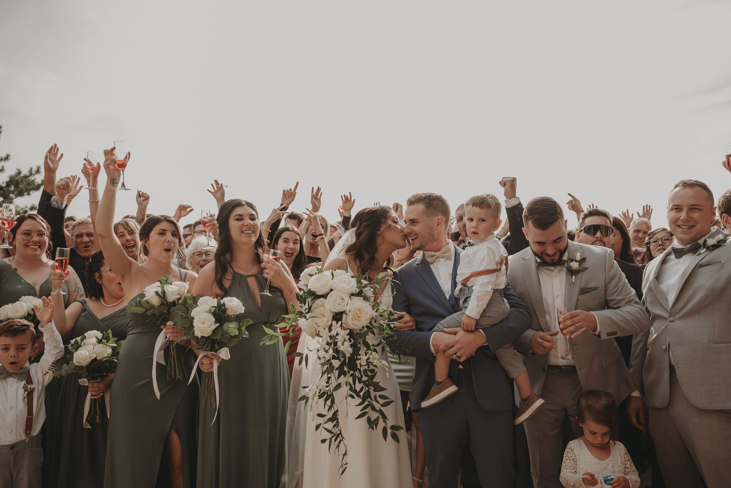Wedding party celebrates outdoors with raised arms and joyful expressions.