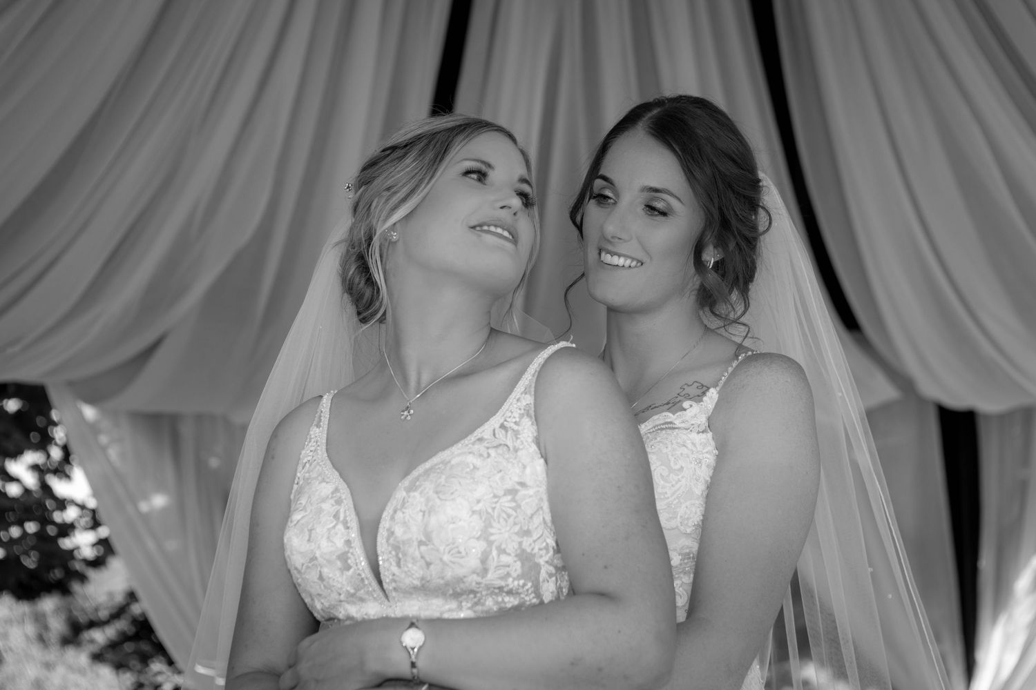 A black and white wedding portrait with draped fabric backdrop and elegant white dresses.