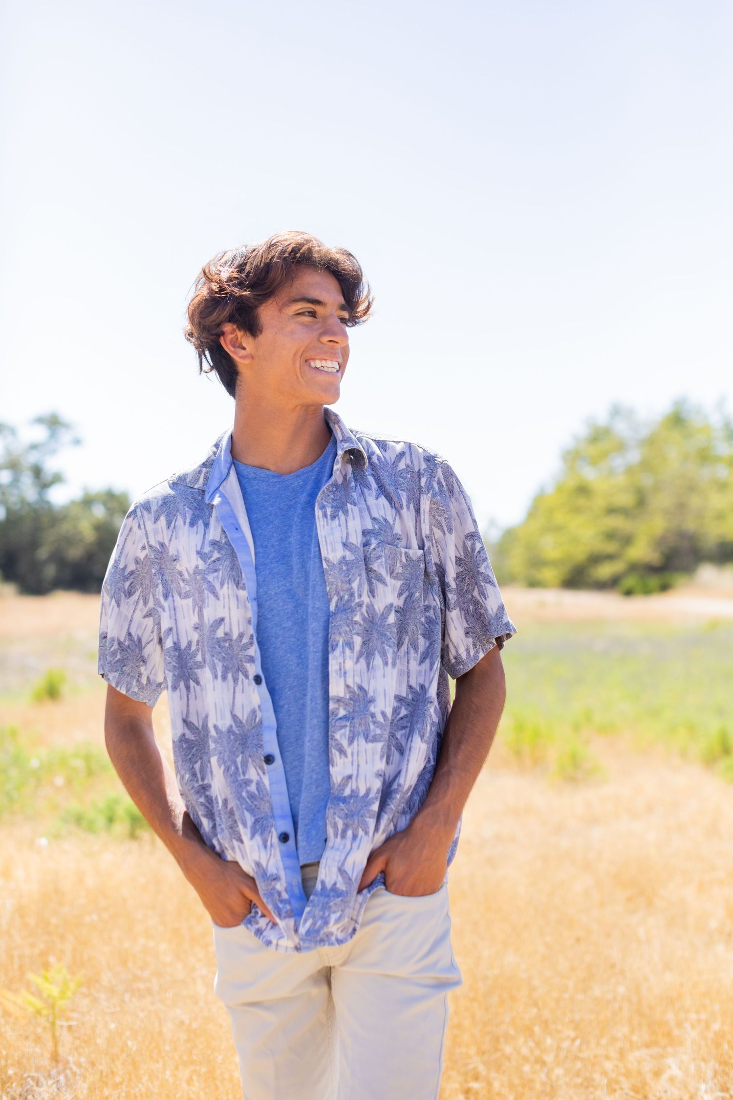 A high school senior in blue Hawaiian shirt and khakis standing in sunny field.